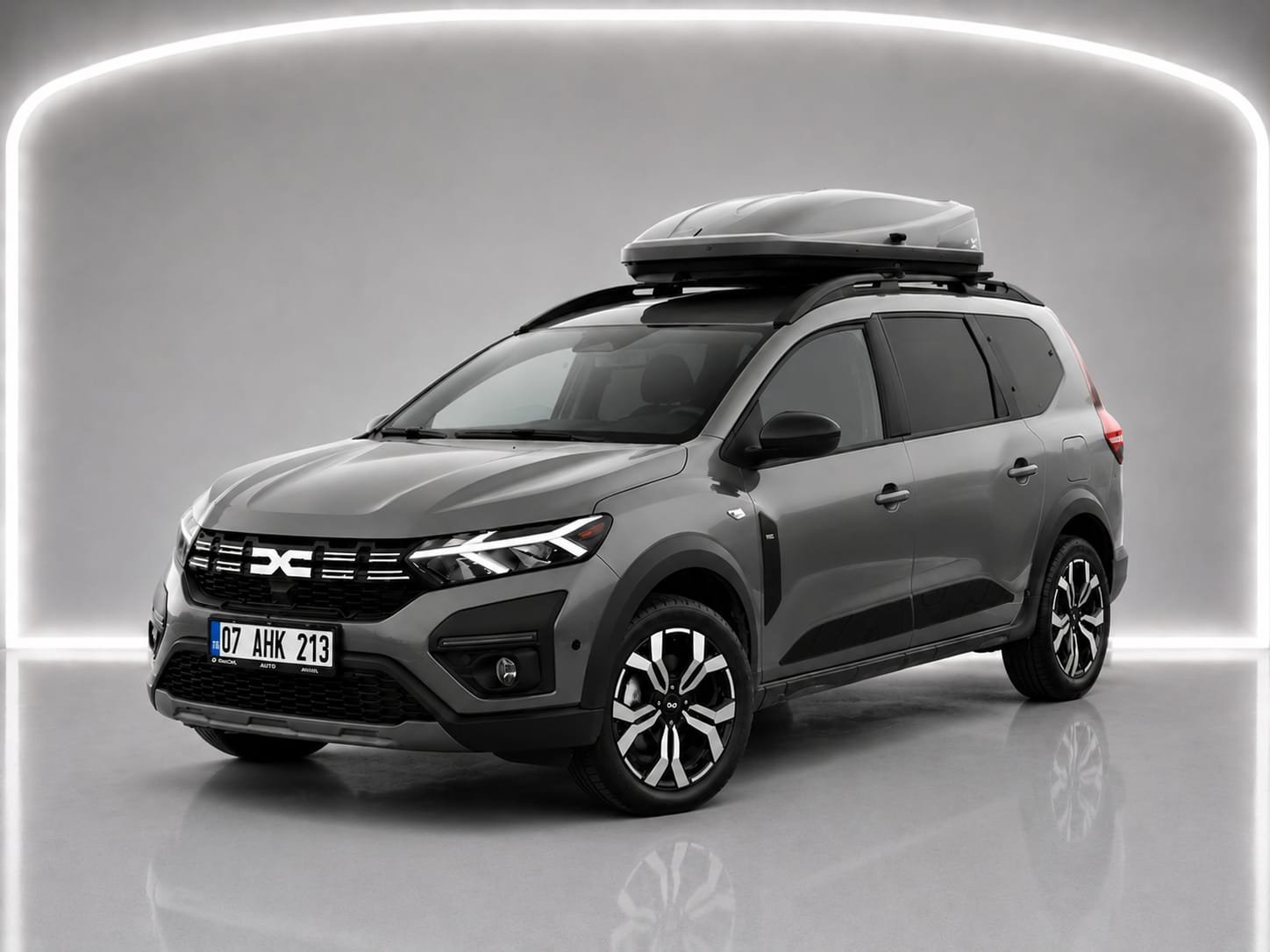 Grauer Dacia Jogger A/T mit Dachbox in einer Studioaufnahme