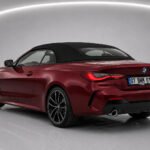 Red 2023 BMW 430i Cabrio car with black soft top in studio setting rear view