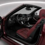 Driver side interior of a 2023 BMW 4.30i Cabrio with red leather seats and open roof